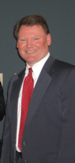 Jim Greenwald with a black suite and a red tie smiling