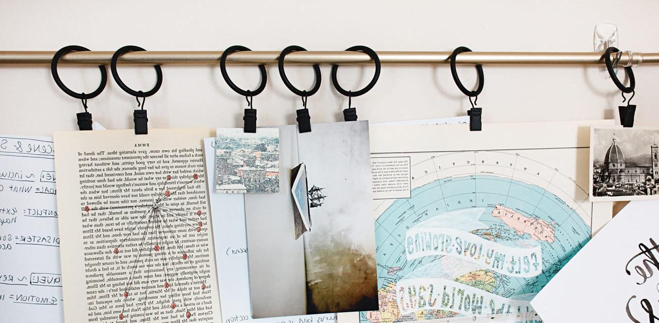 Photos, maps and printed pages hanging from clips on a curtain rod