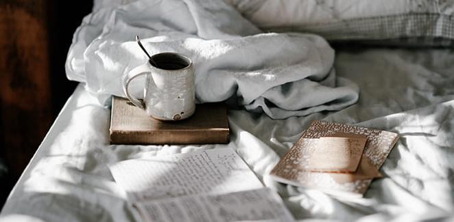 Books, notebooks, and a coffee cup sitting on a bed